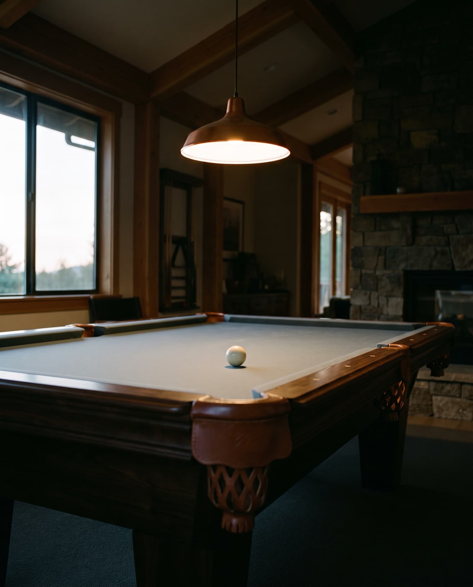A restored pool table under a pendant light, a single cue ball sitting still on the cloth